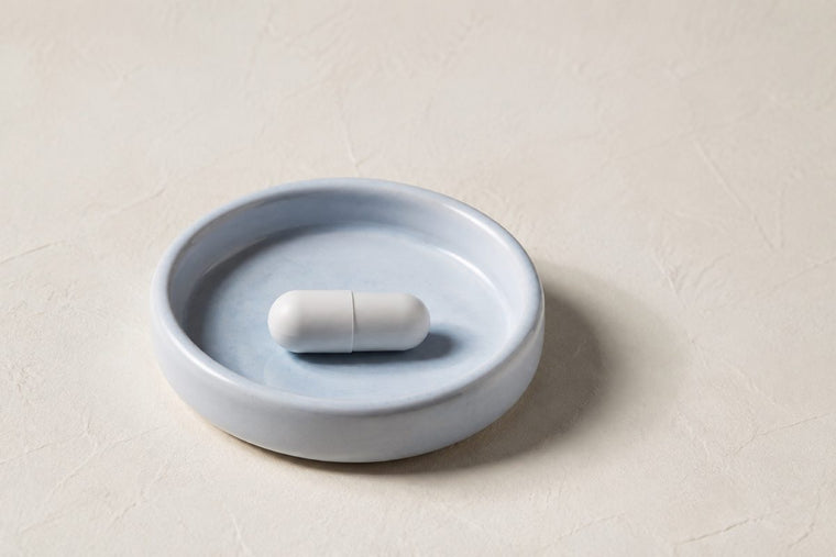 One capsule resting in a shallow light blue dish with a raised rim